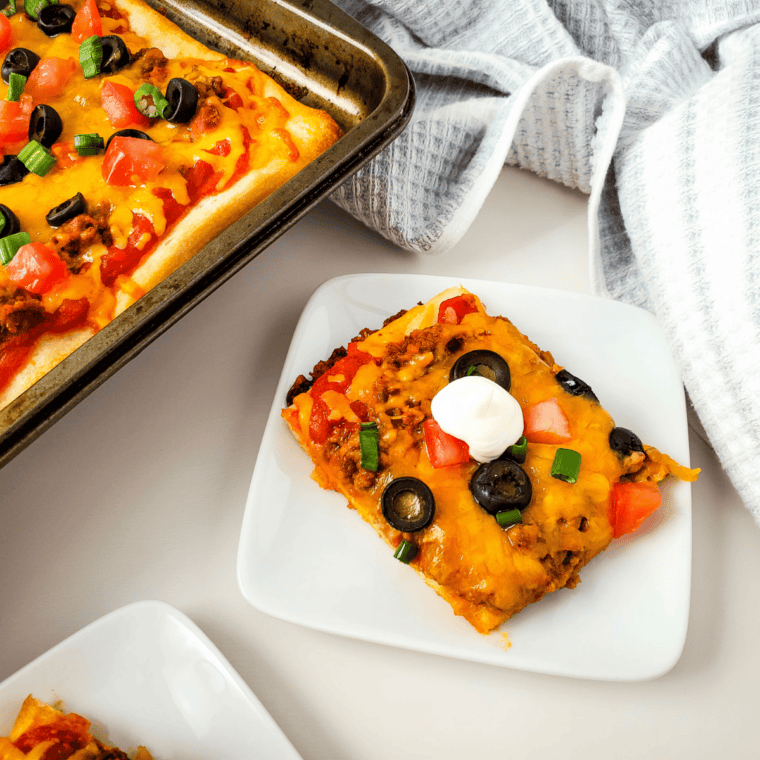 Easy taco pizza on a baking sheet topped with ground beef, cheddar, olives, tomato, and green onion