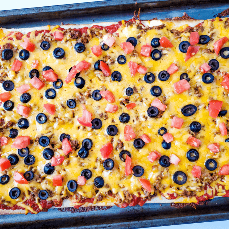Finished taco pizza topped with diced tomato, green onions, and a dollop of sour cream, sliced and ready to serve