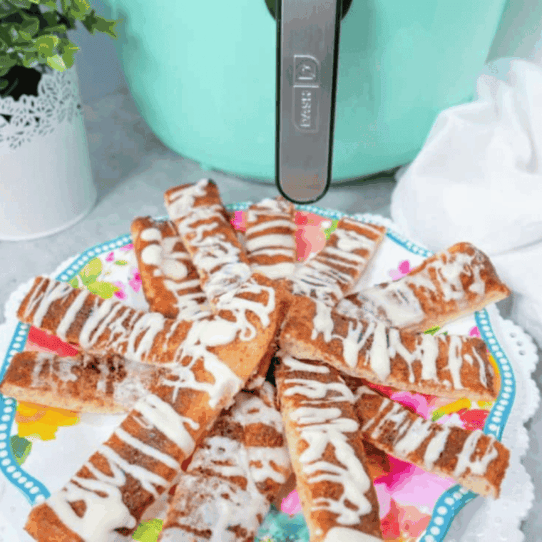 A basket of golden-brown air fryer cinnamon sticks heavily coated in cinnamon sugar with a side of white icing.