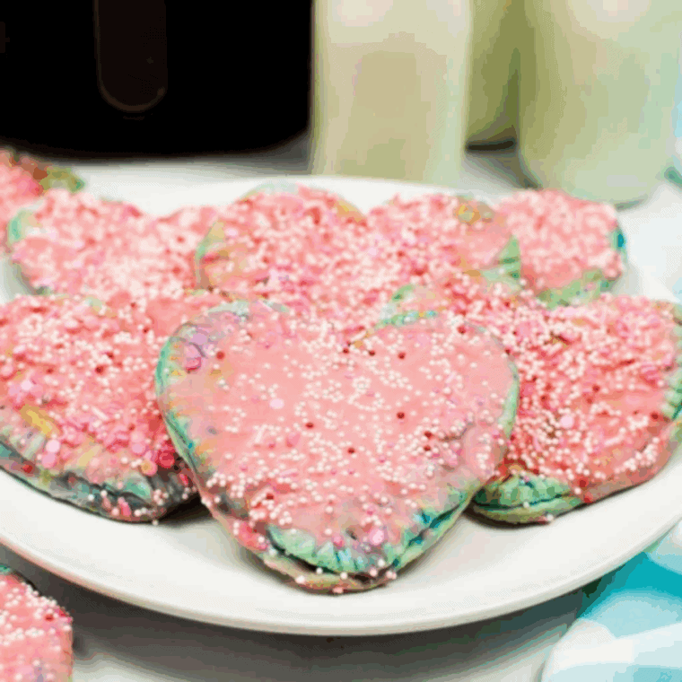 Heart-shaped air fryer pop-tarts decorated with pink icing and sprinkles on a plate.