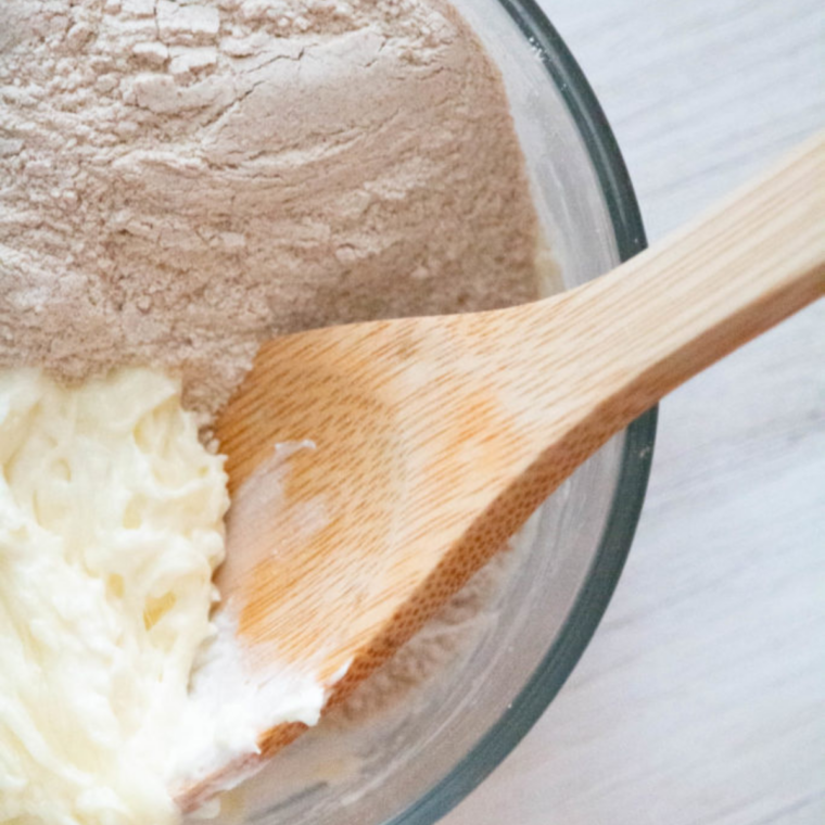 Almond flour and egg being mixed into warm, melted cheese batter in a bowl.
