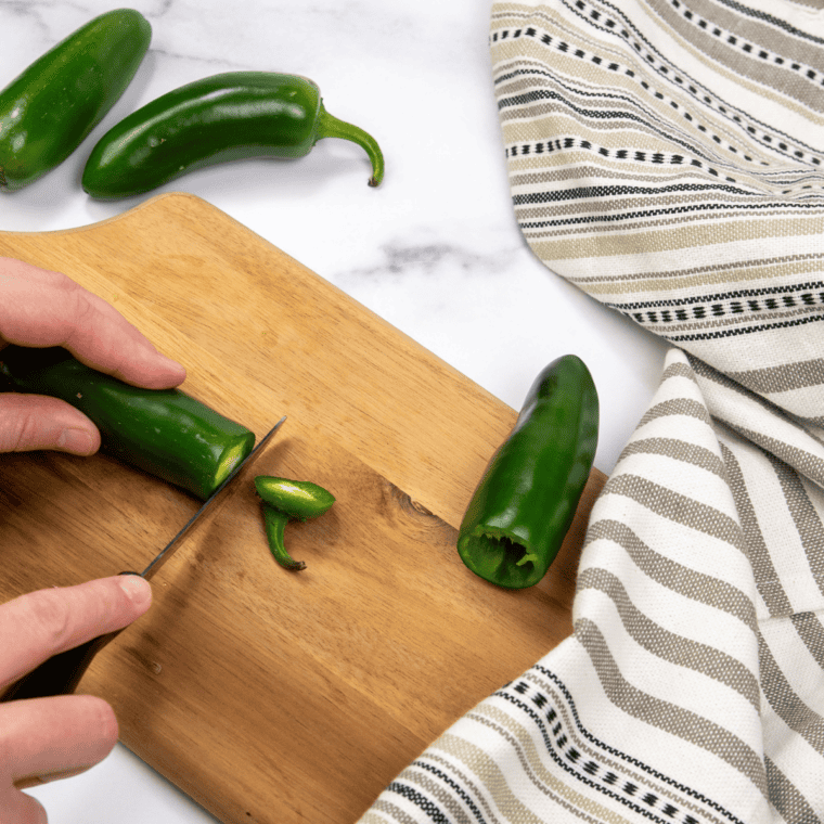 Fresh jalapeño peppers being boiled in a pot after removing stems and seeds.