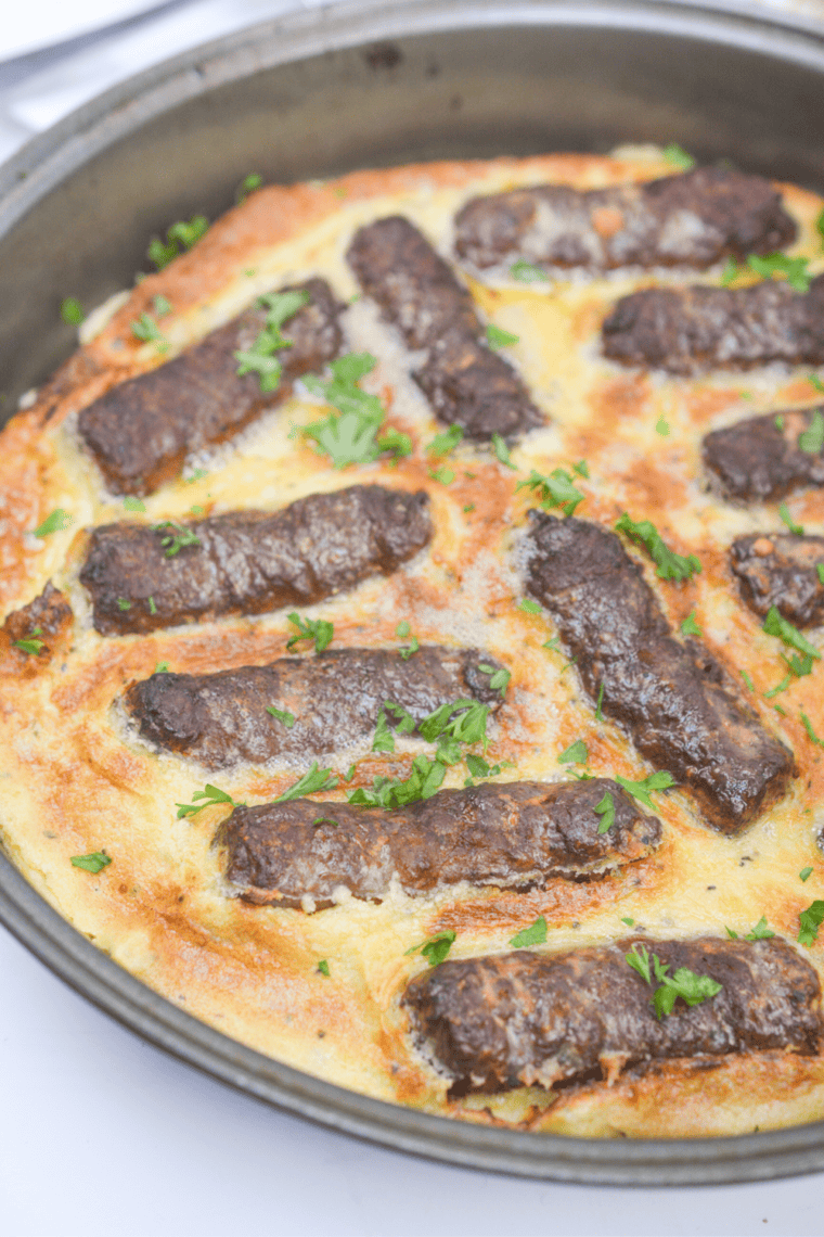 Close-up of air fryer toad in the hole served in a small black dish, sausages poking out of risen golden batter