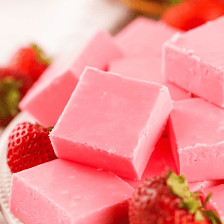 Stack of smooth pink strawberry fudge cubes on a white plate with fresh strawberries.