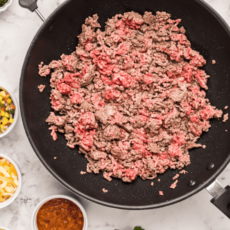 Ground beef browning and crumbling in a skillet for copycat Del Taco tacos