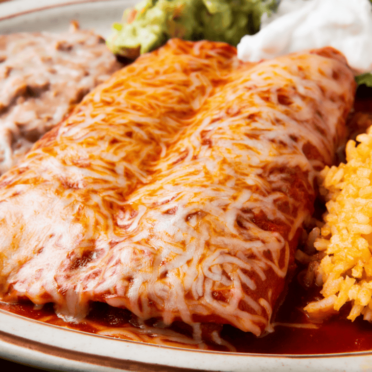 Baked Instant Pot chicken enchiladas garnished with sour cream, guacamole, and cilantro