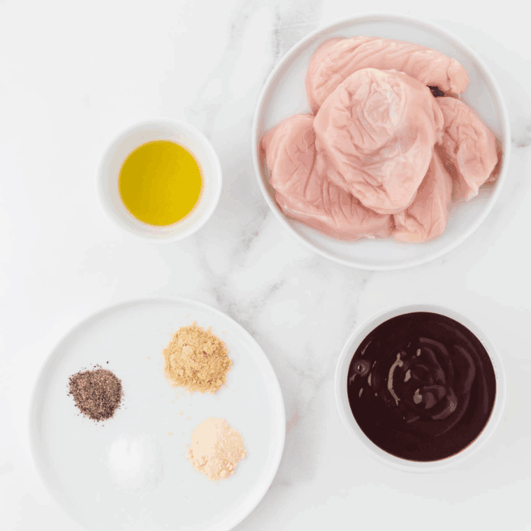 Ingredients for Crock Pot BBQ pulled chicken — chicken breasts, barbecue sauce, brown sugar, mustard, and spices laid out on a kitchen counter.