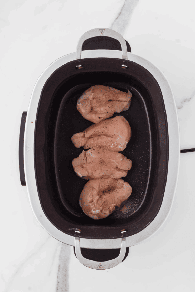 Boneless skinless chicken breasts arranged in a single layer in the bottom of a slow cooker.