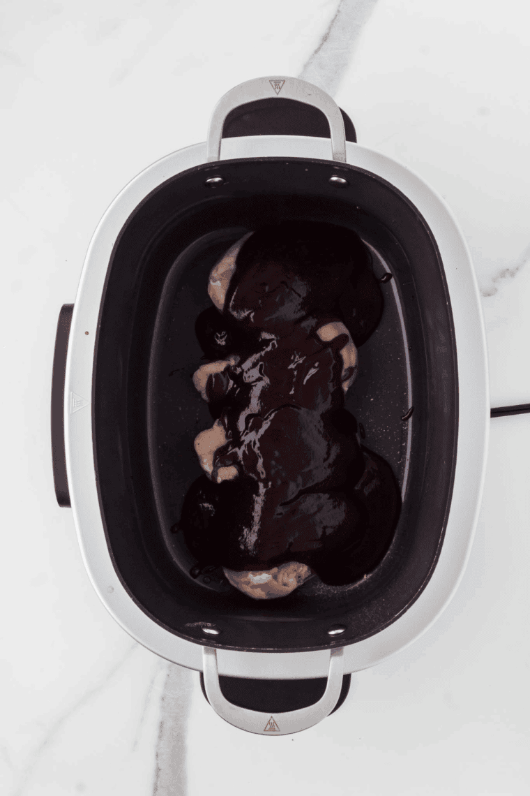 Homemade barbecue sauce mixture being poured over raw chicken breasts in the Crock Pot.