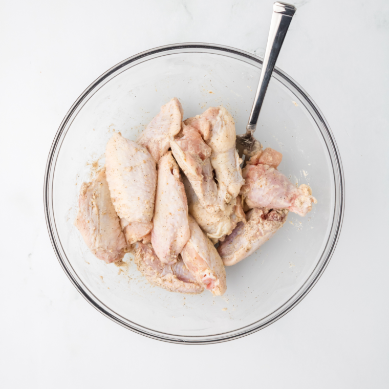 Raw chicken wings tossed with Chinese seasoning blend in a glass mixing bowl.