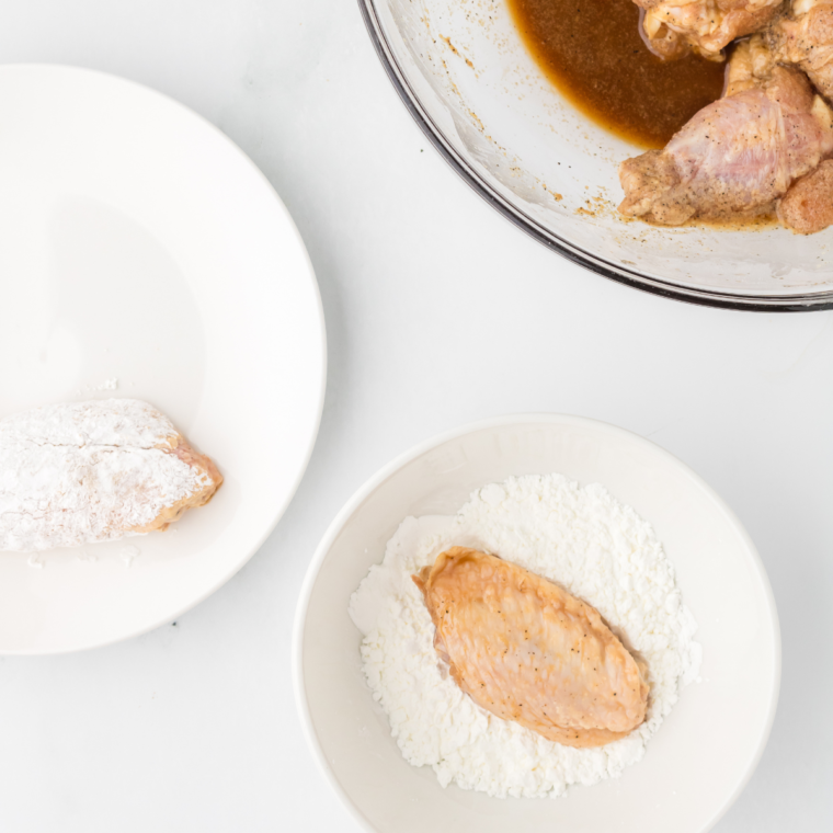 Dredging chicken wings in cornstarch and potato starch for a crispy coating.