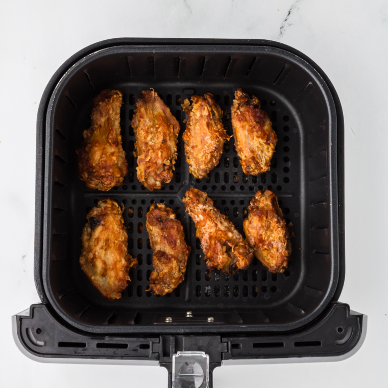 Chinese chicken wings crisping in the air fryer basket halfway through cooking.