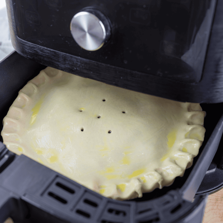 Placing the assembled cherry pie into the air fryer basket to bake until golden.