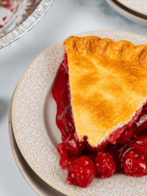 Slice of air fryer cherry pie on a white plate with a scoop of vanilla ice cream