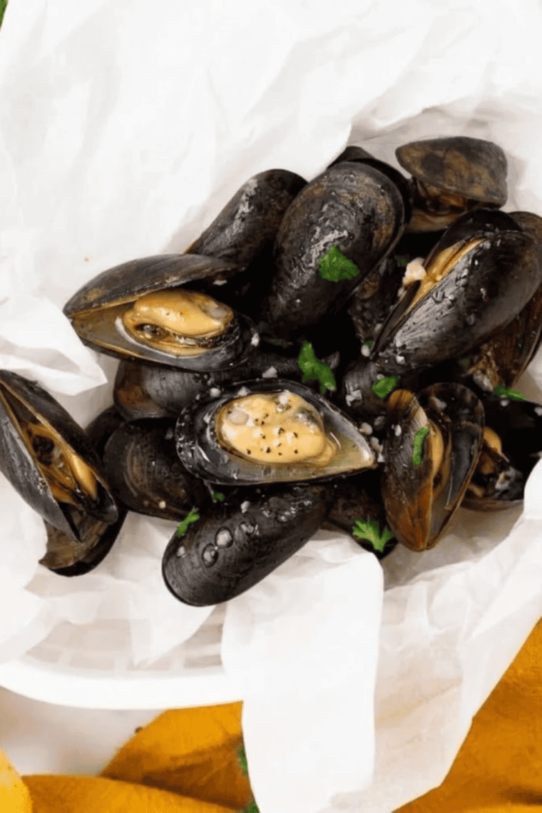 Air fryer mussels in garlic butter sauce garnished with herbs, served hot with bread for dipping.