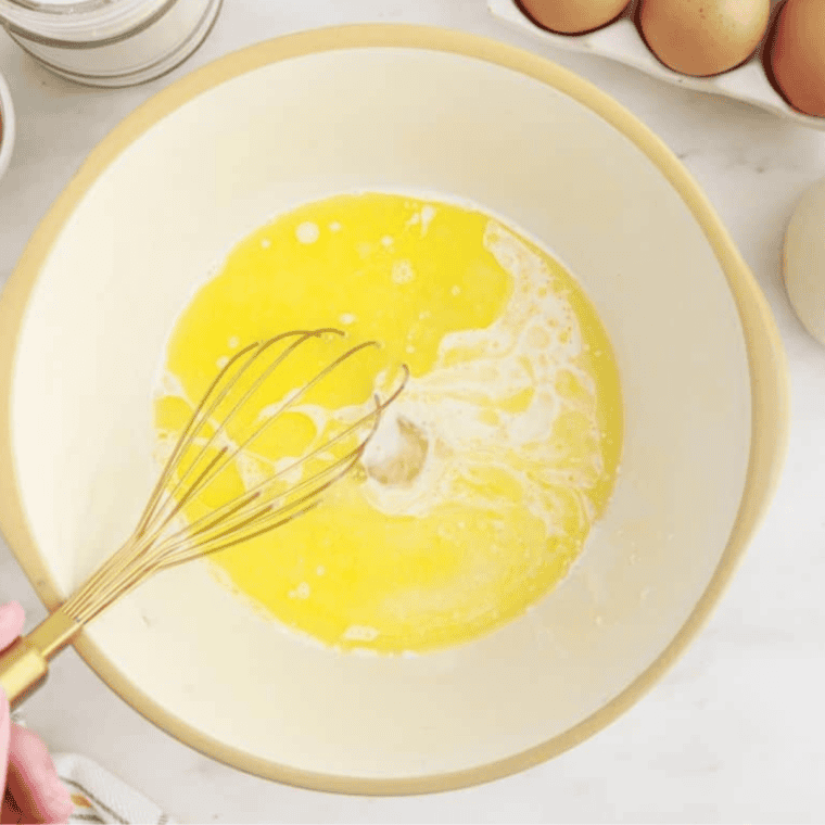 Whisking honey, sugar, eggs, heavy cream, and melted butter in a bowl for corn casserole