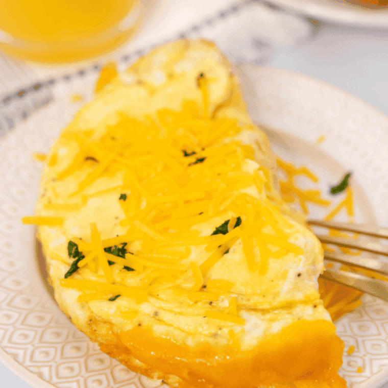 Golden, fluffy air fryer cheese omelette folded on a plate with melted cheese inside and garnished with herbs.