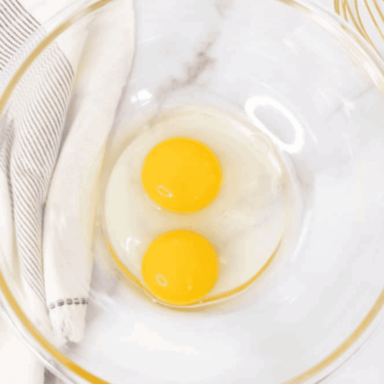 Whisked eggs in a small bowl with salt and pepper sprinkled on top, ready to cook.