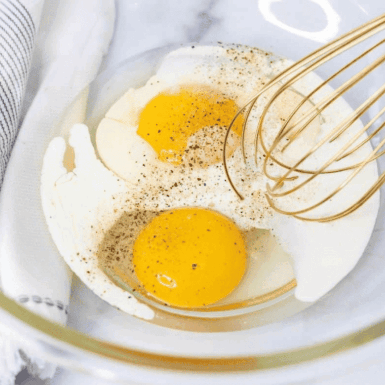 Cracked eggs being whisked in a bowl with seasoning for an air fryer omelette.