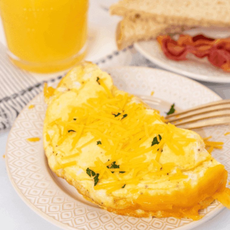 Fluffy air fryer cheese omelette folded on a plate with gooey melted cheddar and fresh herb garnish.