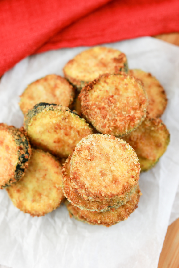 Crispy air fryer zucchini zircles golden brown on a plate served with dipping sauce and fresh herbs