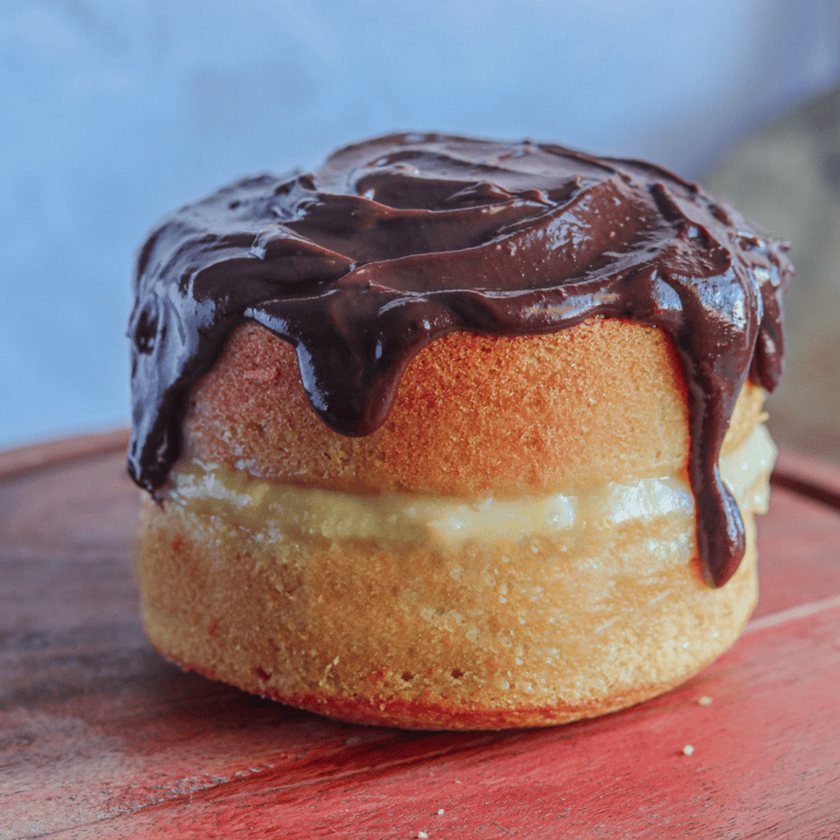 Air Fryer Boston Cream Pie with two layers of golden cake, creamy pastry filling, and chocolate ganache drizzle on top, served on a white plate.