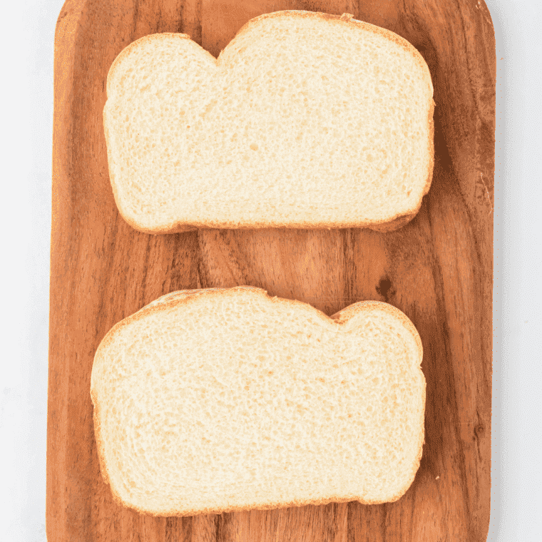 Overhead of two slices of white bread on a wooden chopping board