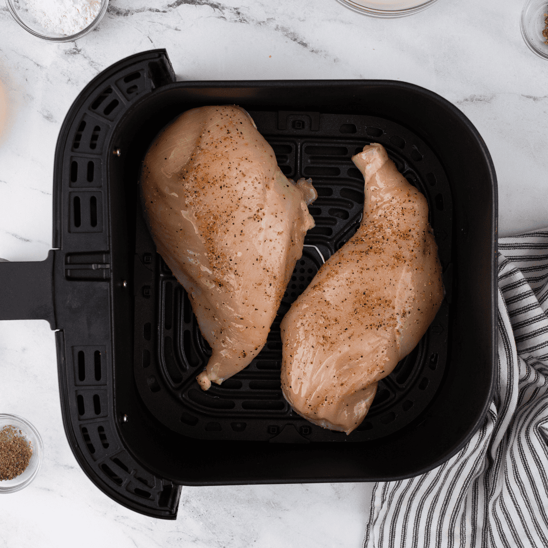 Raw chicken breasts seasoned and soaking in buttermilk marinade in a glass bowl