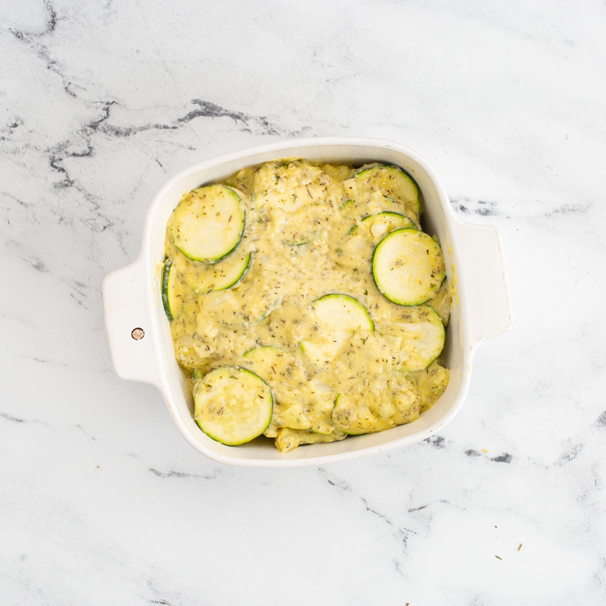 Spooning zucchini casserole mixture into a greased air fryer pan