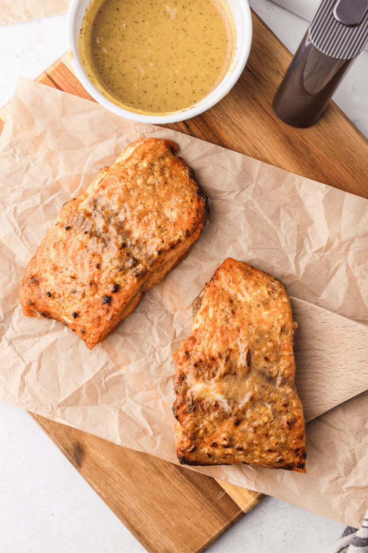 Air fryer honey mustard salmon cooked and plated with a small bowl of honey mustard sauce beside it.