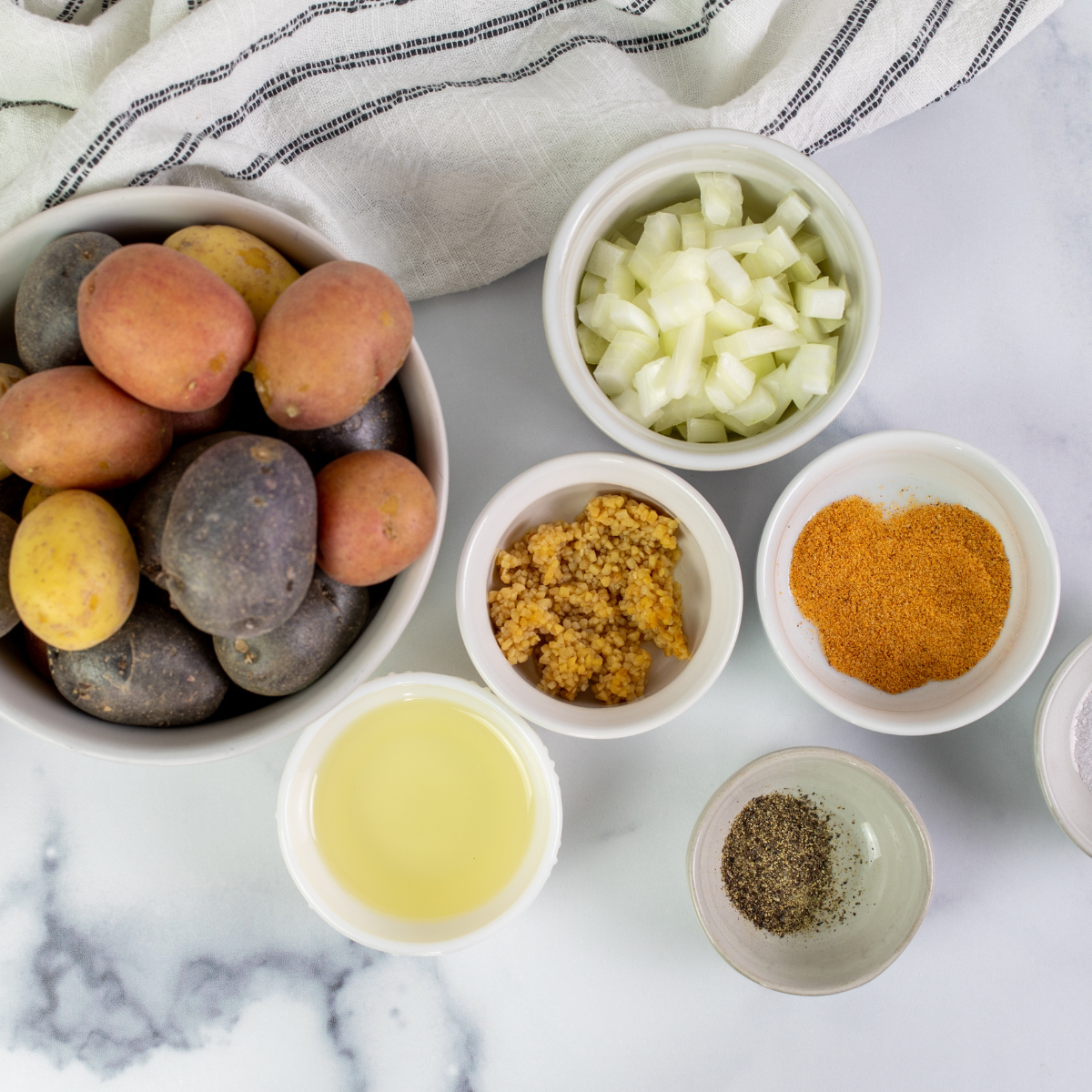 Ingredients for Air Fryer Roasted Bacon Potatoes on a table: Russet or Gold Potatoes, Olive Oil, Salt, Black Pepper, Shredded Cheddar Cheese, Crumbed Cooked Bacon, and Chives.