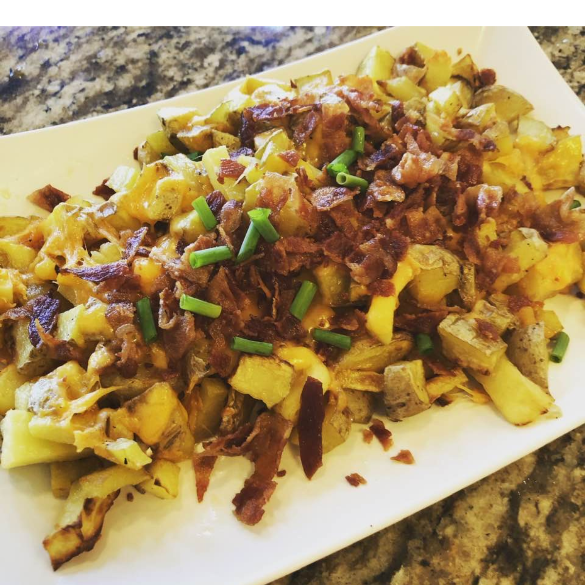 Crispy roasted potatoes removed from the air fryer, topped with shredded cheddar cheese and crumbled bacon."