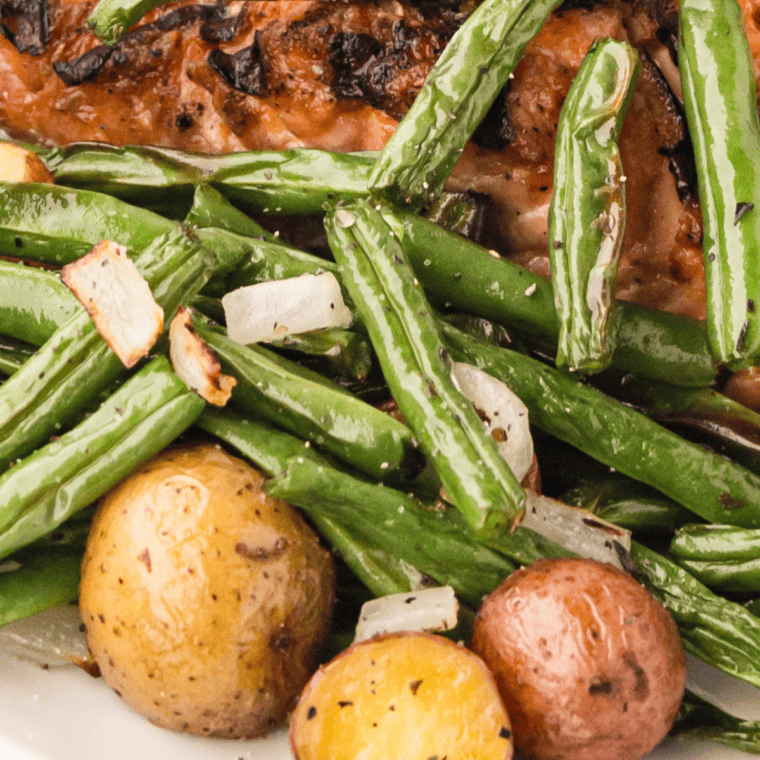 Seasoned green beans and diced potatoes cooked in the air fryer until crispy and golden, served on a plate.