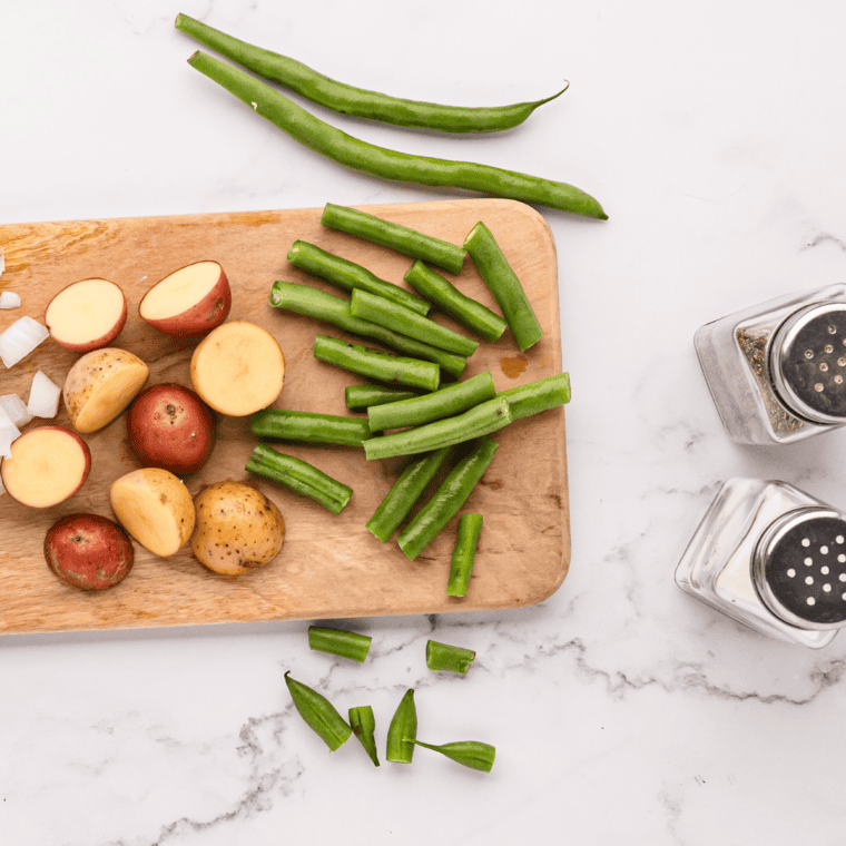Fresh green beans being trimmed and potatoes diced into uniform chunks for even cooking.