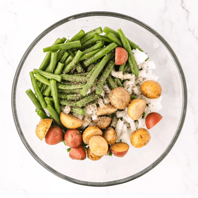Green beans and diced potatoes tossed with seasonings and olive oil in a large mixing bowl, ready for air frying.