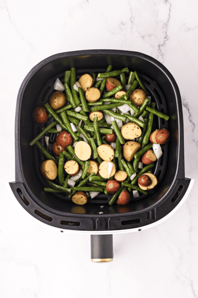 Seasoned green beans and potatoes placed in an air fryer basket in a single layer, ready to cook at 380°F.