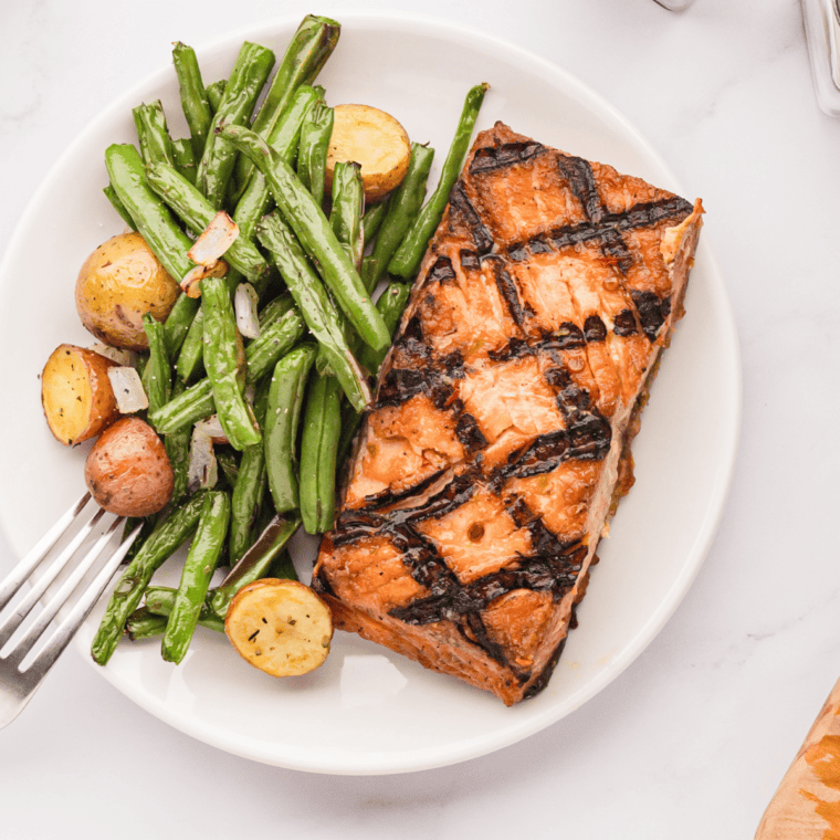 Golden roasted potatoes and crisp green beans cooked in the air fryer and served on a white plate.