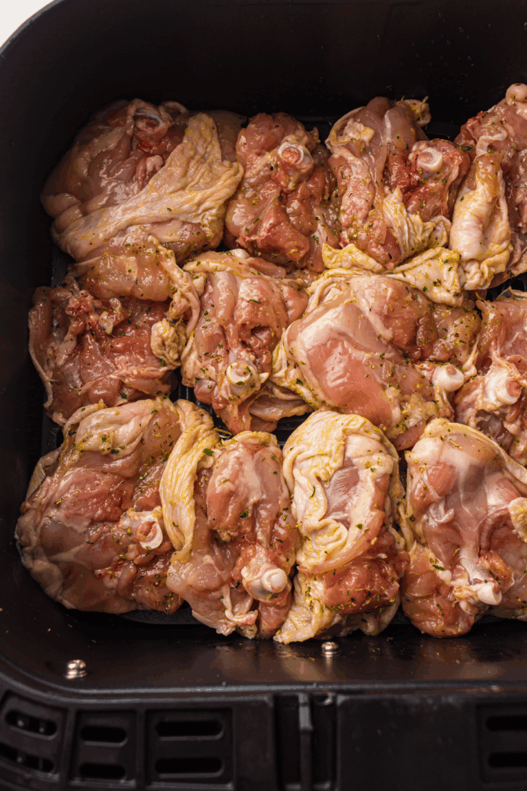 Coated chicken thighs arranged in a single layer in the air fryer basket, cooking at 360°F and flipped halfway for even browning.