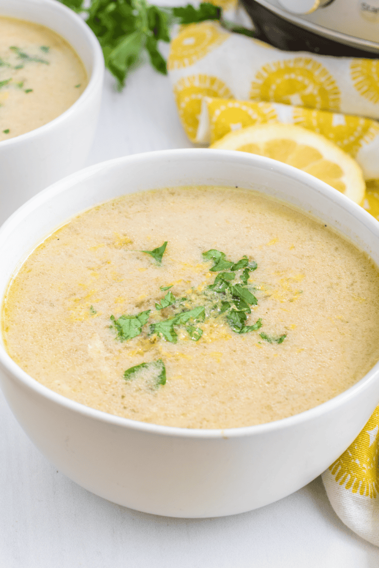 Instant Pot Greek lemon chicken soup garnished with fresh dill and lemon in a white bowl, spoon resting on the side