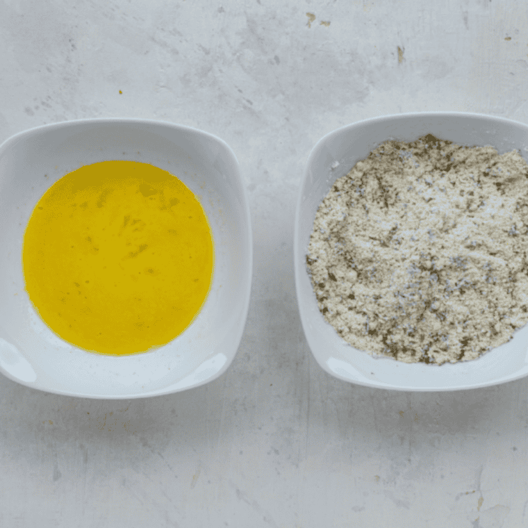 Dredging stations prepared with egg, lemon juice, garlic powder in one bowl, and flour, parmesan cheese, parsley, salt in another; chicken dipped in egg mixture then coated in flour mixture, placed into air fryer basket.