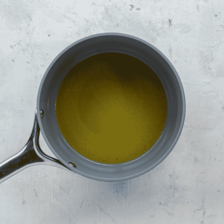 Butter, lemon juice, and chicken broth simmering gently in a saucepan, stirred occasionally until melted.
