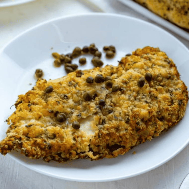 Golden-brown air fryer chicken piccata topped with lemon-caper sauce, garnished with fresh parsley on a white plate.