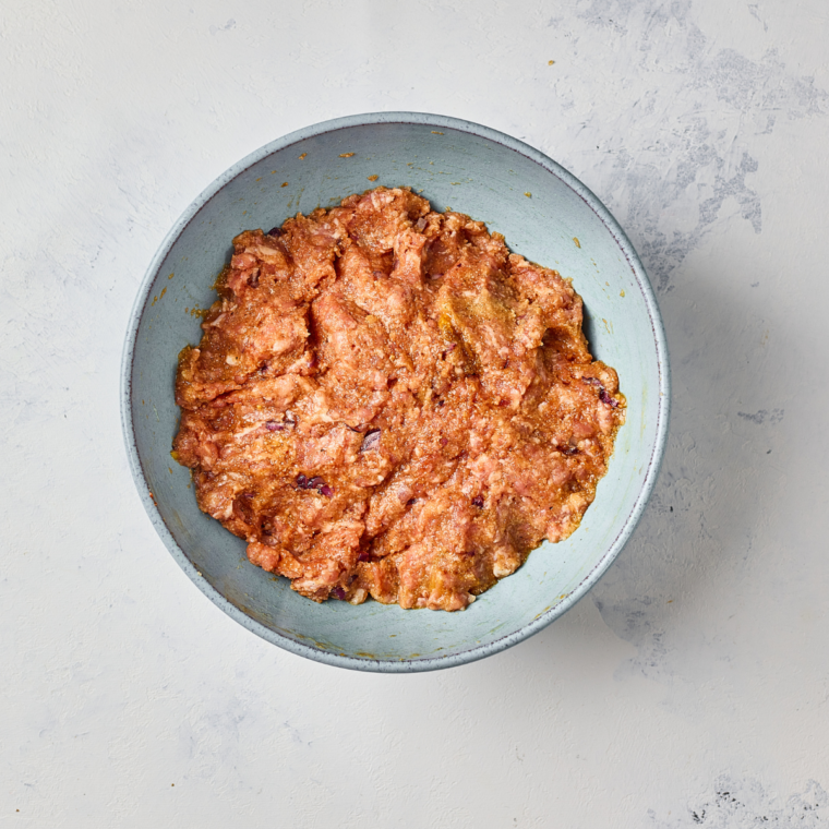 Hand mixing ground beef with panko and grated ginger in a glass bowl