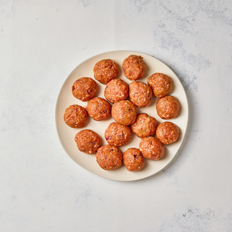 Rolling a one-inch meatball between wet hands beside a tray of finished ones