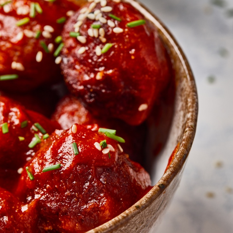 Spooning glaze over cooked meatballs in the air fryer basket before the second cook