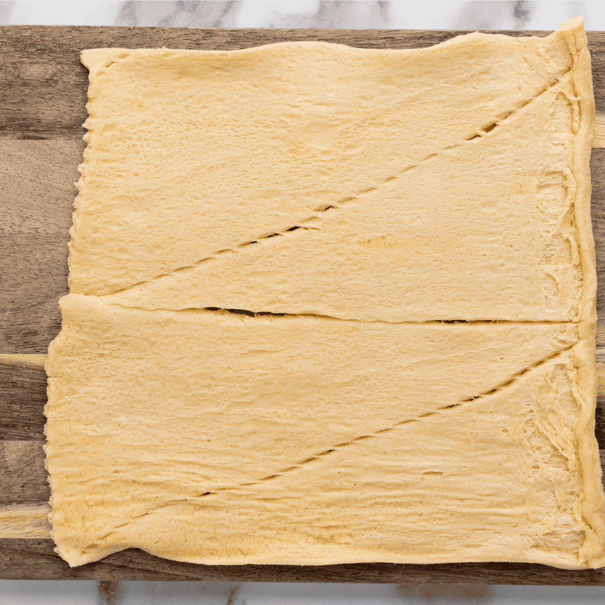 "Preparation of Air Fryer Pigs in a Blanket: sausage links wrapped in dough on a cutting board."