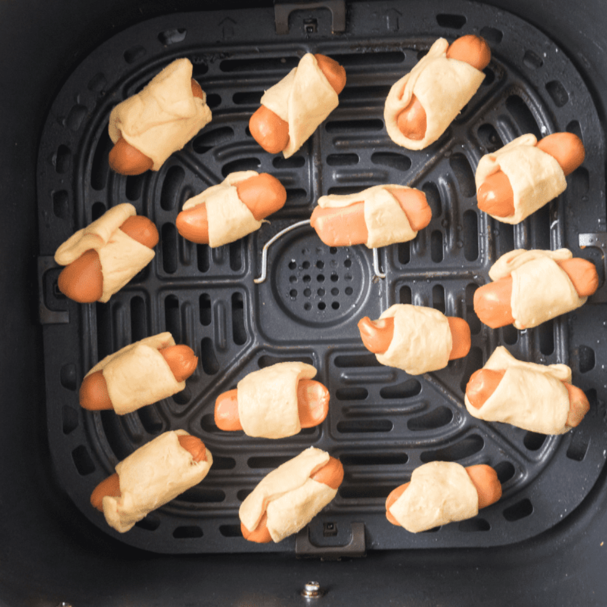 "Air fryer basket filled with uncooked Pigs in a Blanket, ready to be cooked."
