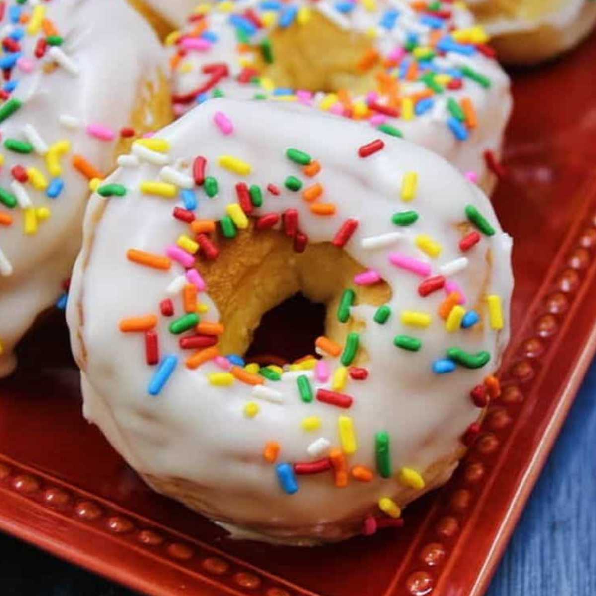 Homemade Dunkin’ Donuts sprinkle donuts topped with glaze and rainbow sprinkles on a cooling rack.