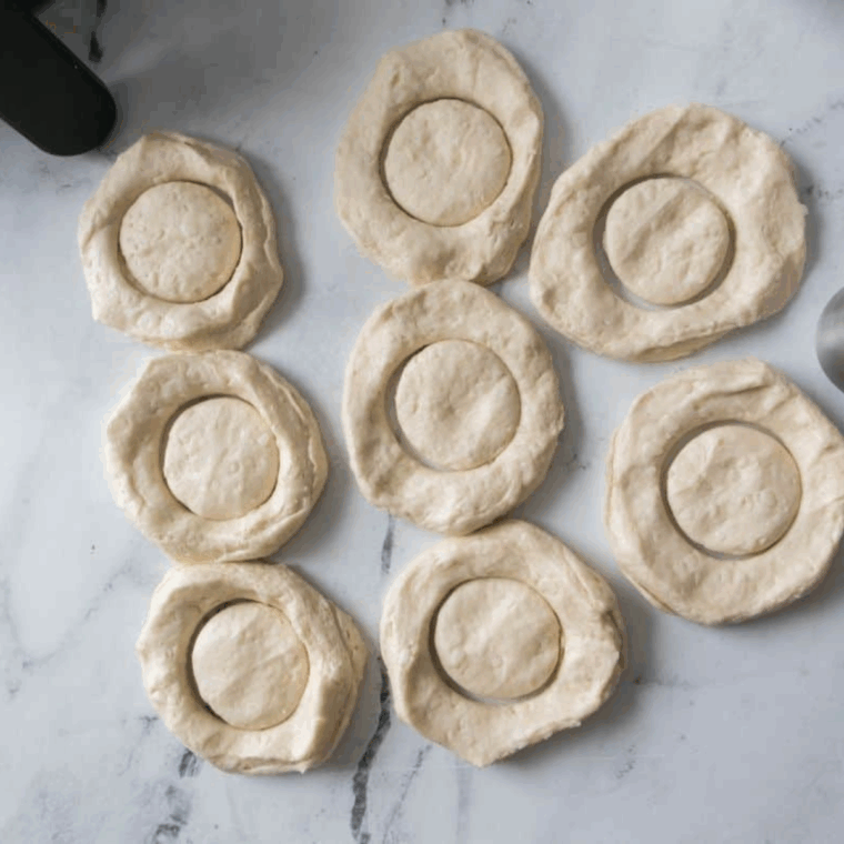 Using a biscuit cutter to cut out the centers, creating donut shapes and mini donut holes for baking.