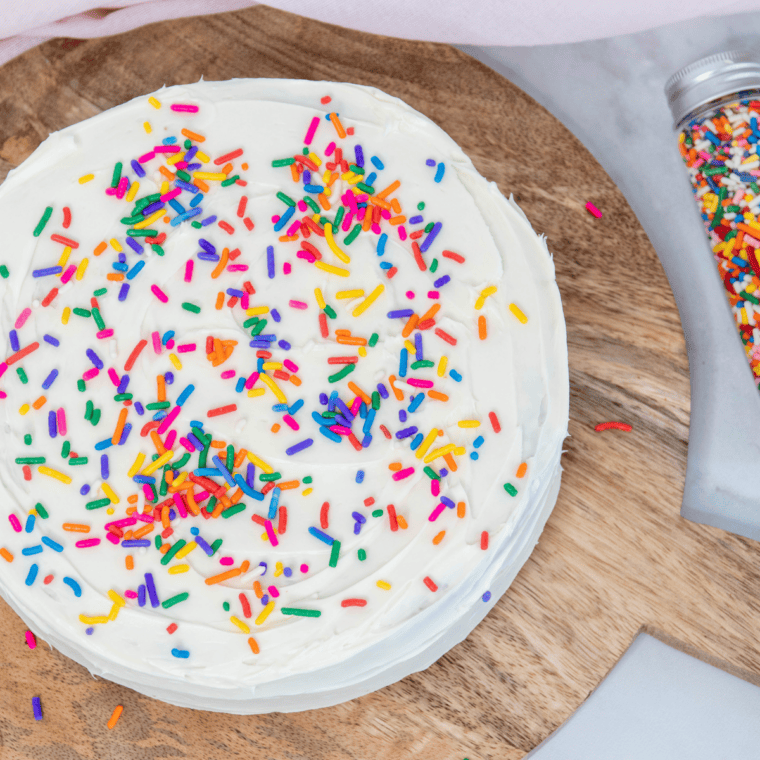 Air fryer birthday cake frosted with vanilla frosting, rainbow sprinkles, and birthday candles